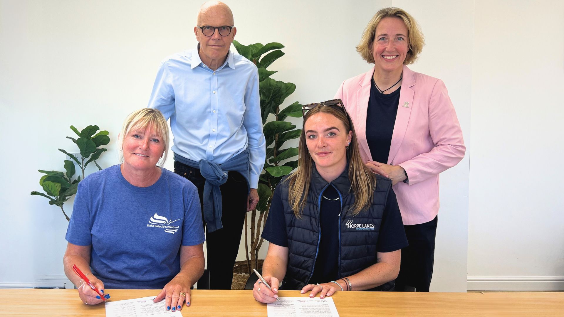 Four people smile at the camera, two standng and two sitting. They represent British Water Ski and Wakeboard, and have just signed the Brighton Plus Helsinki Declaration. 